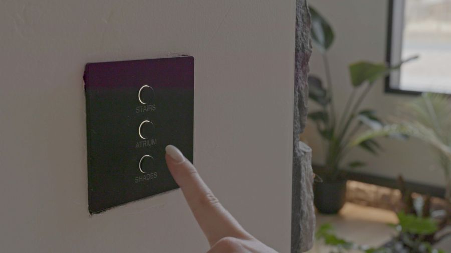 A hand tapping a smart lighting wall keypad.