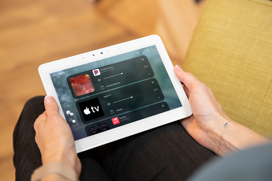 Person holding a tablet with smart home AV control system, managing music and Apple TV across multiple rooms.